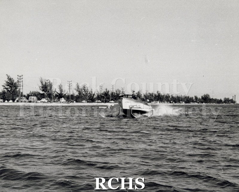 Black and white photograph of "High Pockets" in the water with three men aboard.