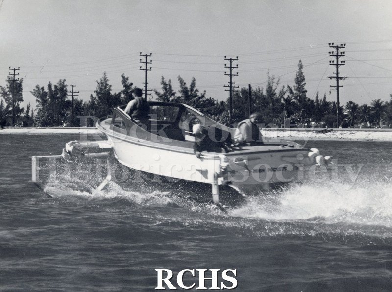 Black and white photograph of "High Pockets" with three men aboard. The boat is moving away from the camera.