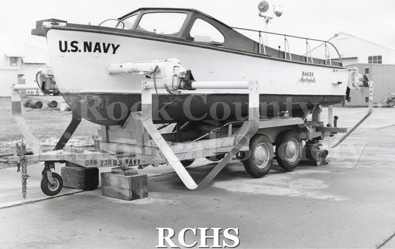 Black and white photograph of "High Pockets" on a trailer. The words: "U.S.Navy" are visible on the front. The word "Baker Hydrofoils" is visible on the backside.
