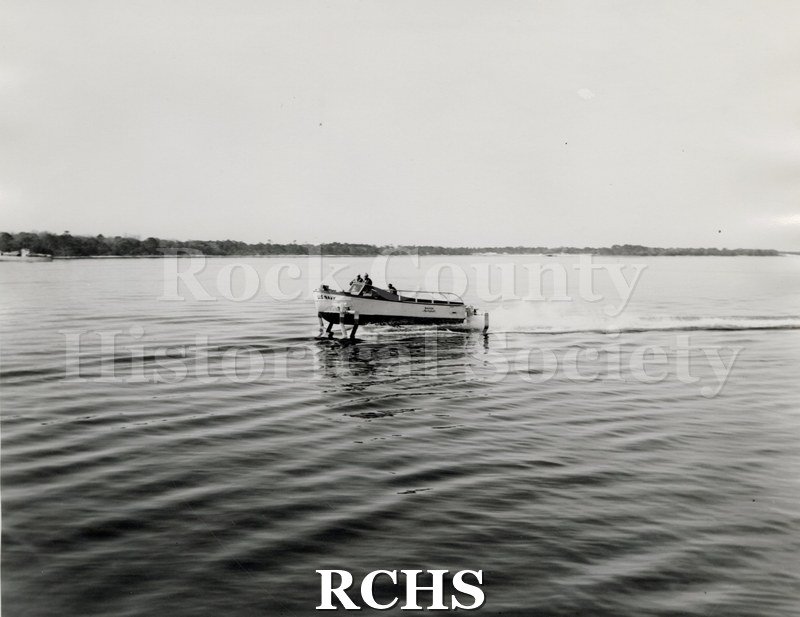 Black and white photograph of "High Pockets" on the water with three men aboard.