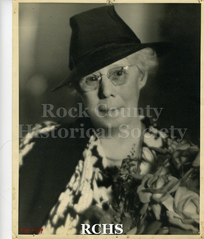 Black and white photograph of Carrie Jacobs Bond. She is wearing a colorful blouse, dark hat and glasses.