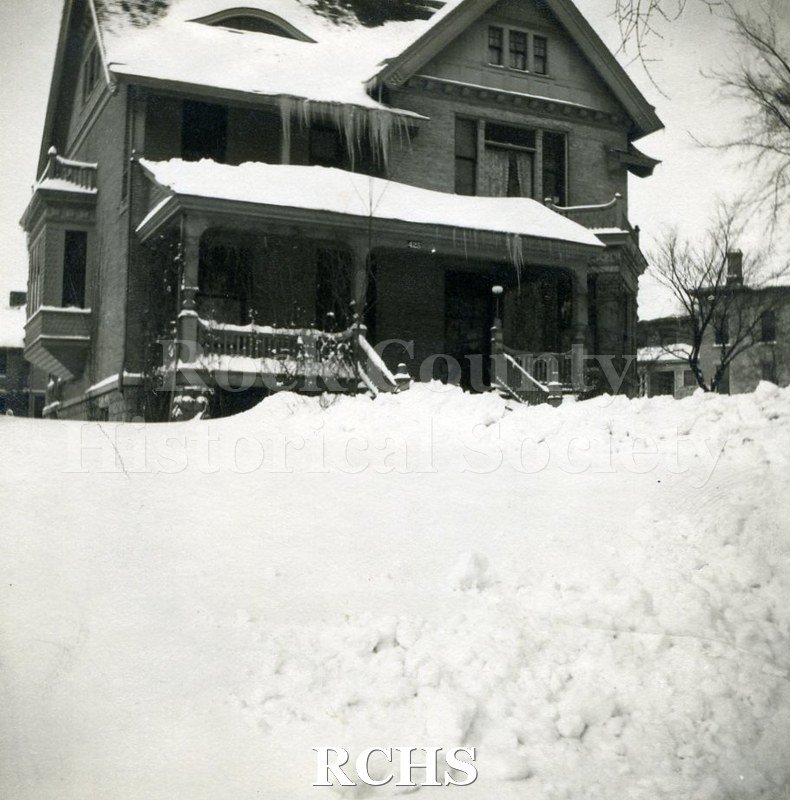 Black and white photograph of Dr. James Mills' Residence, a three story house with a porch along the front of it. There is snow up to the porch steps.