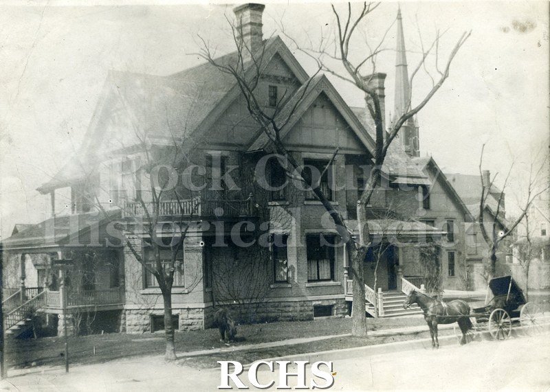Black and white photograph of Dr. James Mills' Residence, a three story house with a front porch and side porch. There is a horse and carriage parked in front of it.