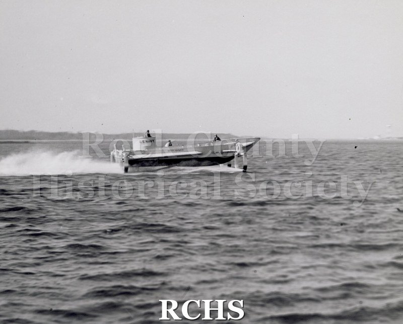 Black and white photograph of "High Lander" in the water. There is a man in the turret which has "U.S.Navy" painted on it.