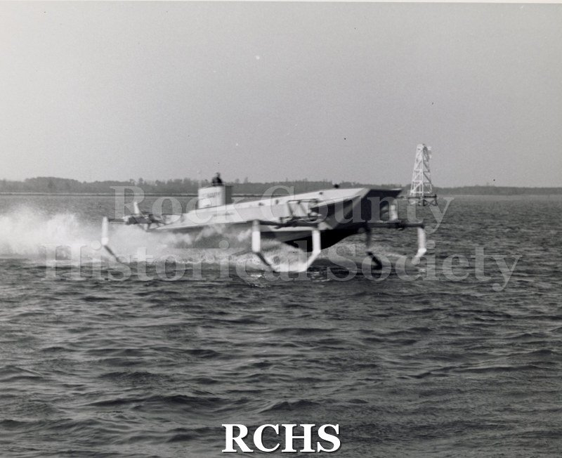 Black and white photograph of "High Lander" in the water. There is a man in the turret which has "U.S.Navy" painted on it.