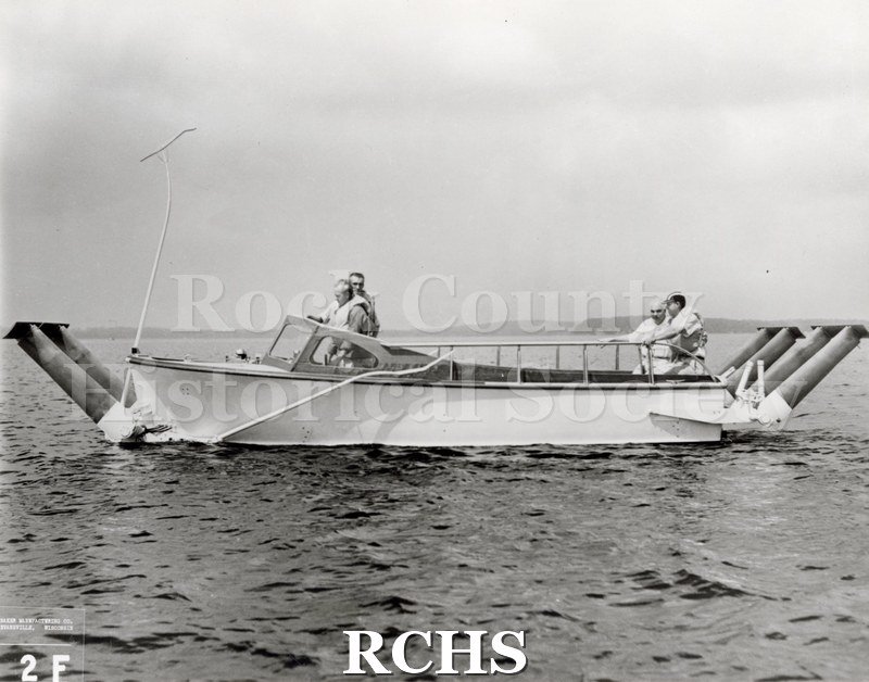 Black and white photograph of "High Tail" in the water with four men aboard. On bottom: Baker Manufacturing Co.