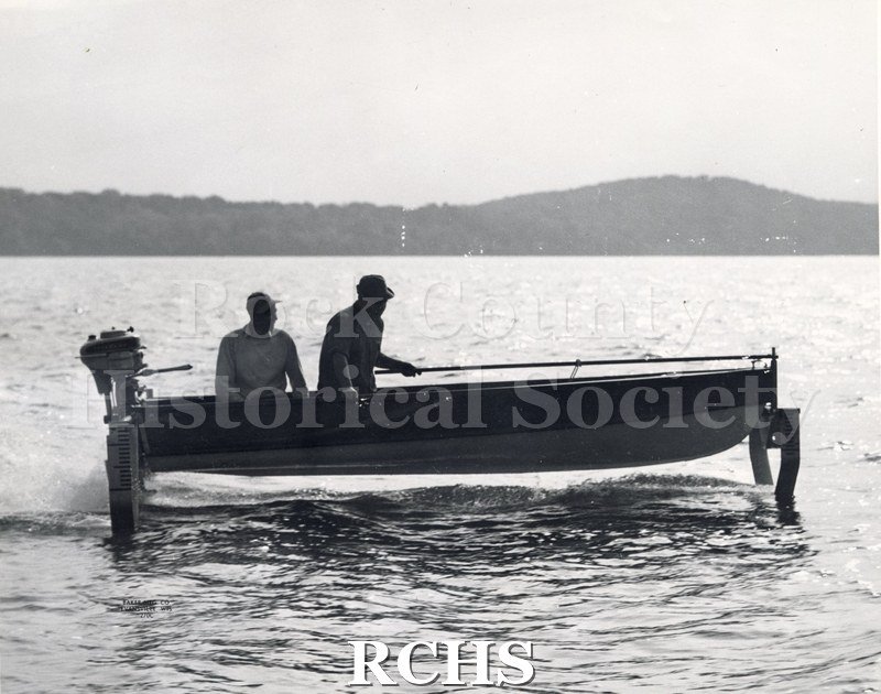 Black and white photograph of a boat with an outdoor motor with two men on board.