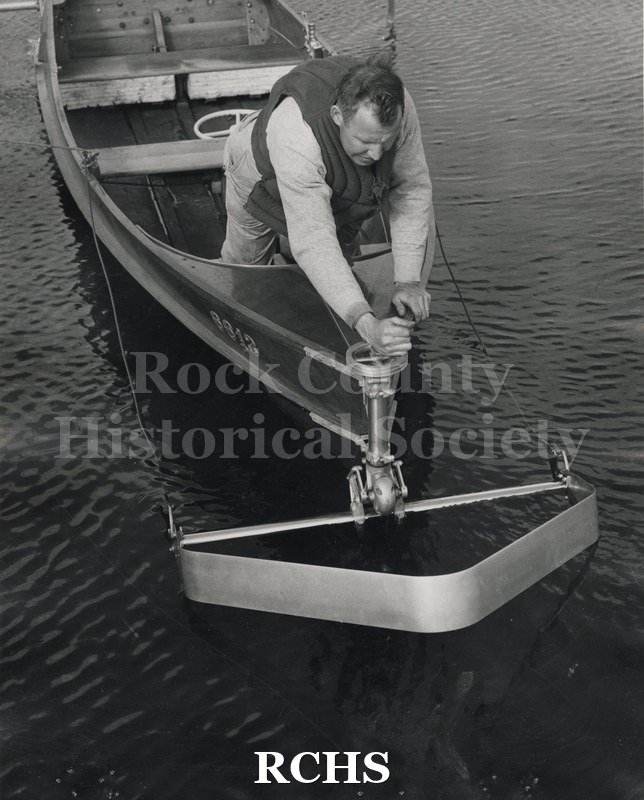 Black and white photograph of an outboard hydrofoil front end view. Man in front is lowering the foil into the water. On separate card: "Max Palmer outboard HF".