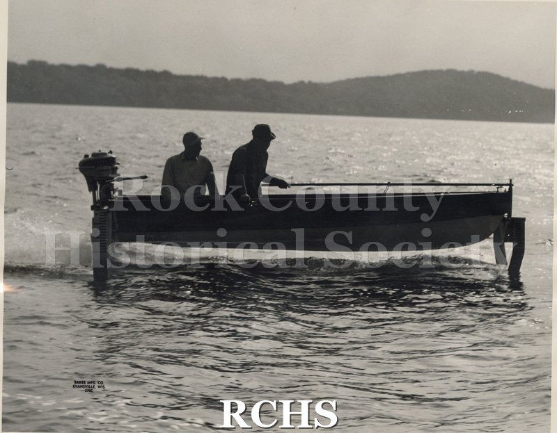 Black and white photograph of two men in an outboard motor hydrofoil boat. Boat is in silhouette. Photographer: Arthur M.