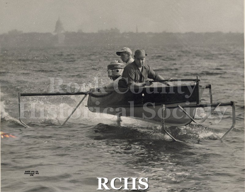 Black and white photograph of a close-up of two men in an outboard motor hydrofoil boat.