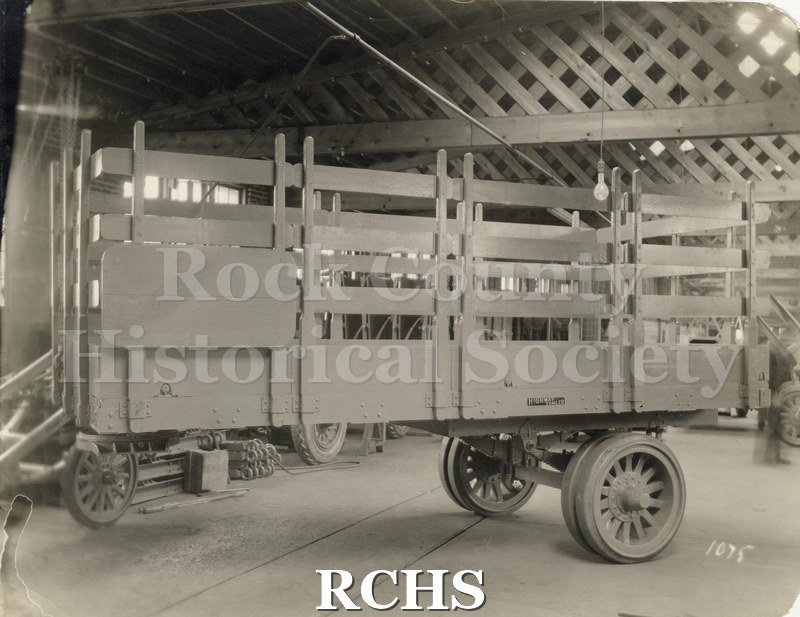 Black and white photograph of the first semi-trailer built by Highway Trailer Co., Edgerton, WI. Shows an empty trailer in a building.