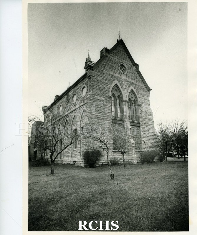 Black and white photograph of Memorial Hall at Beloit College. It is a stone, neo-gothic building surrounded by small trees.