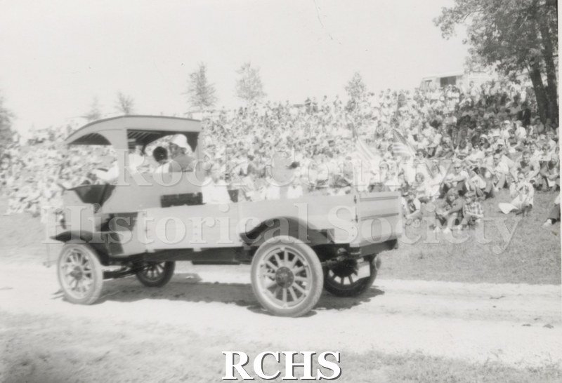 Black and white photograph of a Samson truck being driven along a road with a crowd of people sitting and watching.