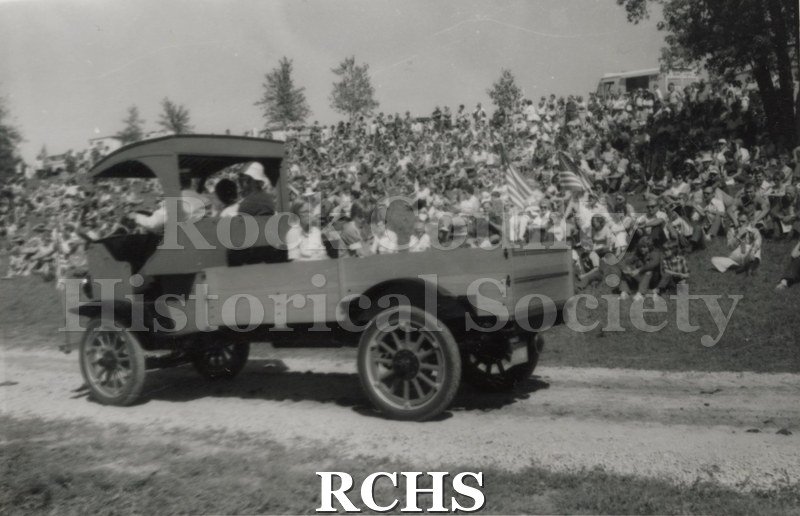 Black and white photograph of a Samson truck being driven along a road with a crowd of people sitting and watching.
