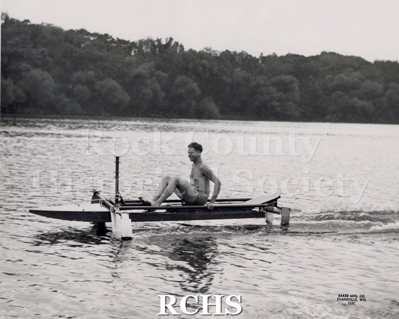 Black and white photograph of Bob Cannon in a hydrofoil boat. On bottom: Baker Mfg. Co. Evansville, Wis.