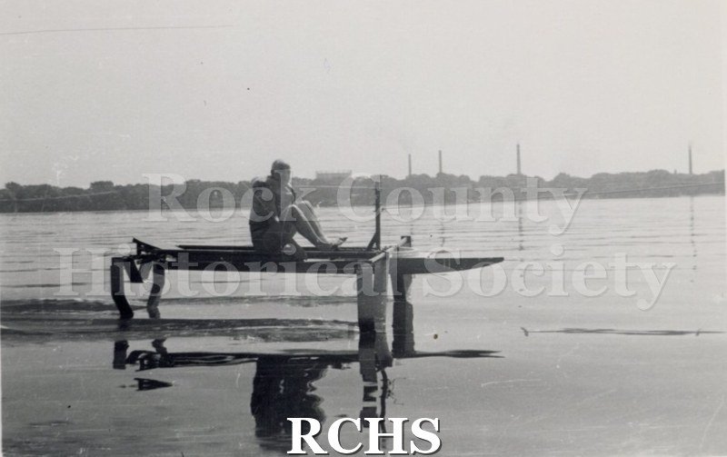 Black and white photograph of Foil Testing. There is a man sitting in a hydrofoil that is stationary. Description given: "Foil testing-J. G.