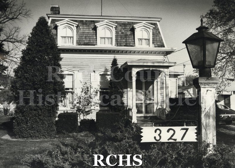 Black and white photograph of 327 Milton Avenue-Howarth House. Shows a two-story house with three evenly spaced windows on the top floor and a porch with the number.