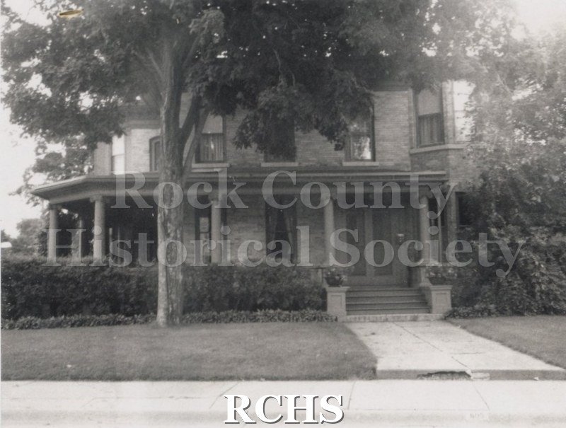 Black and white photograph of the Otto's house, a two story brick house with a front and side porch.