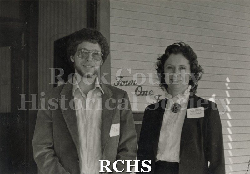 Black and white photograph of two unidentified volunteers standing in front of an unidentified house.