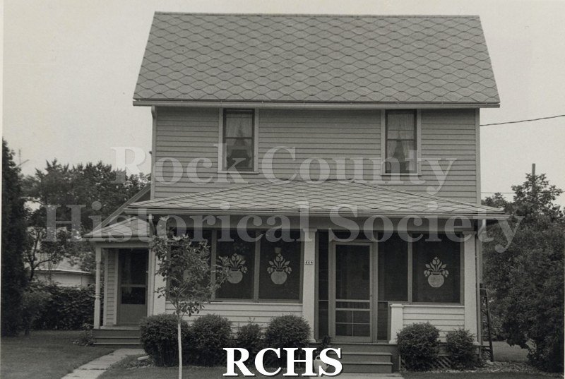 Black and white photograph of the Wickham residence, a two story house with a screened-in porch. Screens have a design on them.