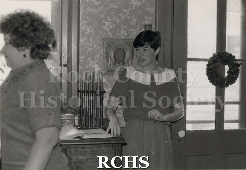 Black and white photograph of the interior of the Tracey home with a volunteer standing near the registration book.