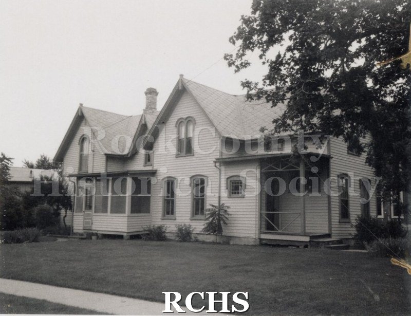Black and white photograph of a two story house with a porch on the right and a glassed in porch on the left at 303 Cornelia.