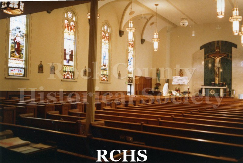 Color photo of the interior of St. Patrick's Catholic Church, Janesville, WI, showing stained glass windows on the left and pews in the middle.