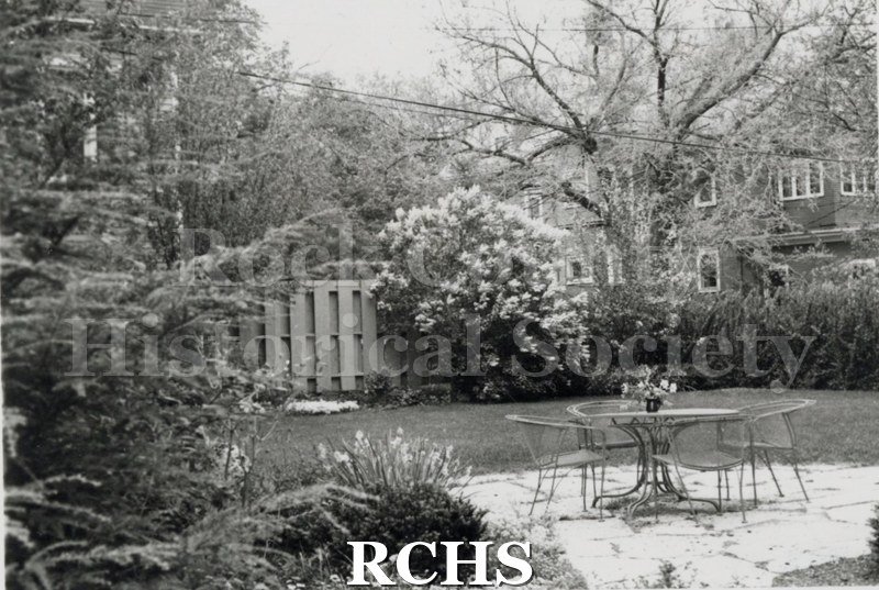Black and white photograph of a patio with a table and chairs on it at the Swanson home.