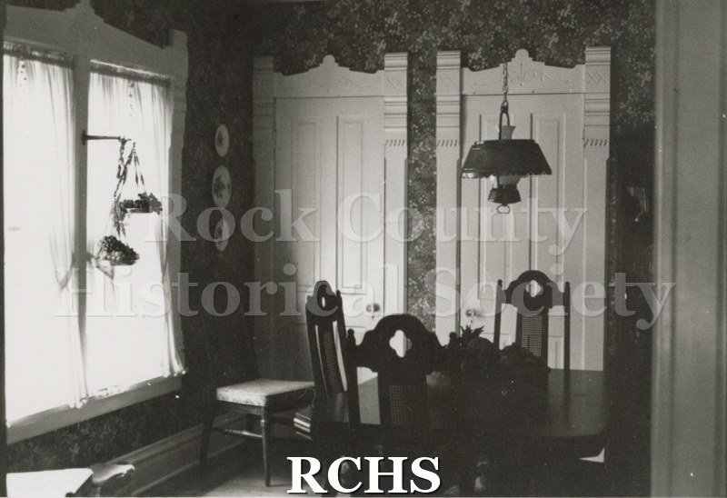 Black and white photograph of the dining room of the Loyd Nelson home with a table and chairs in the middle of the room. A light fixture hangs above the table.