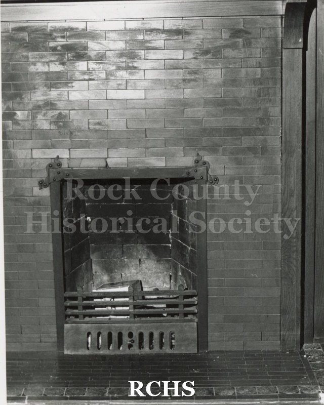 Black and white photograph of the Pliny Norcross-David Holmes residence. Shows a fireplace built into a brick wall. There is a grate in front of it.