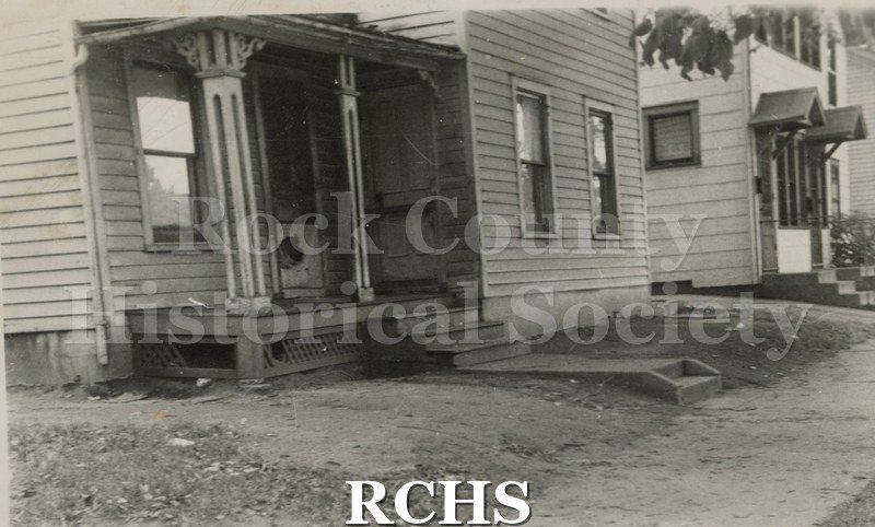 Black and white photograph of a house on West Wall Street, Janesville, WI. Shows a portion of a house with a porch with two pillars.
