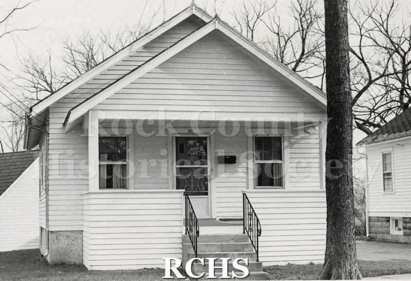 Black and white photograph of 518 Madison St., Janesville, WI. Shows a small one story white house with a porch.
