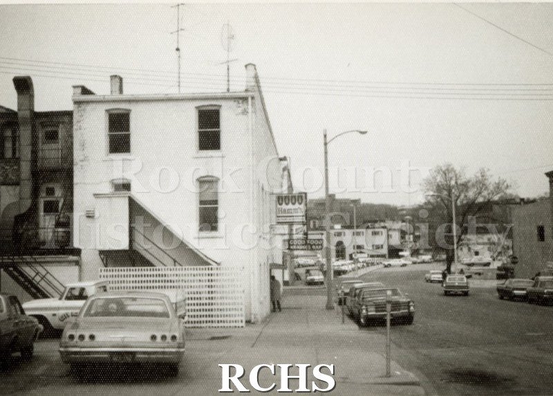 Black and white photograph of Dodge St, Janesville, WI. Shows several Janesville stores.