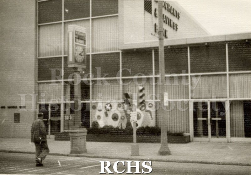 Black and white photograph of the Merchants & Savings Bank with a sign for "Merchants and Savings Bank" on the clock in front of the bank.
