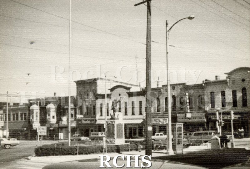 Black and white photograph of Corn Exchange. Shows a row of buildings across from Corn Exchange. The statue is visible in the foreground.