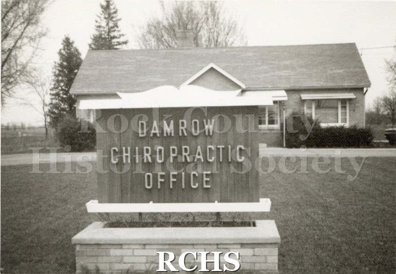 Black and white photograph of Damrow Chiropractic Office. Shows the building in the background and the sign in the foreground.