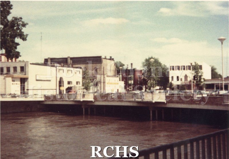 Color photo of the Parking Plaza. Shows the backs of buildings on Main Street with the river in front.