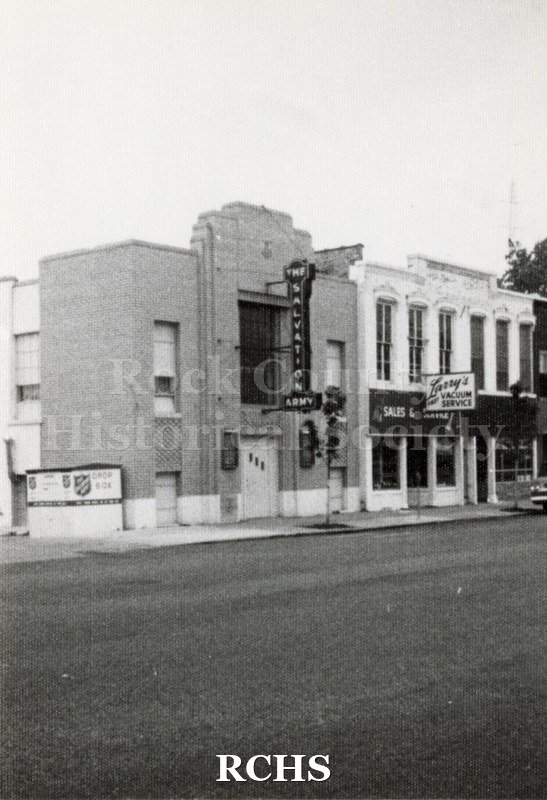 Black and white photograph of two stores in downtown Janesville. On the left is the Salvation Army and on the right is Larry's Vacuum.