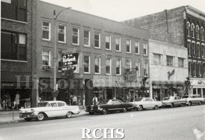 Black and white photograph of stores along Main Street, Janesville, WI., including J. M. Bostwich & Sons; Rexall Drugstore; and Yosts.