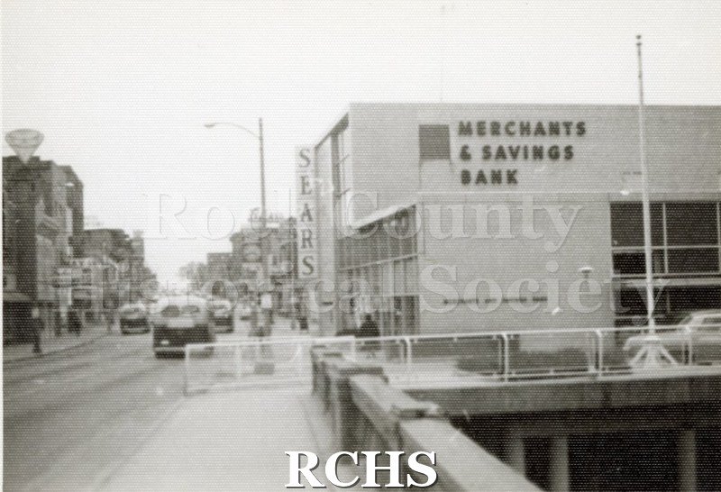Black and white photograph of stores on West Milwaukee Street, especially Merchants & Savings Bank and Sears.
