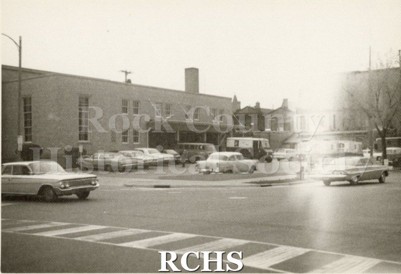 Black and white photograph of the Janesville Post Office, 210 Dodge St., Janesville, WI. Shows mail truck and cars.