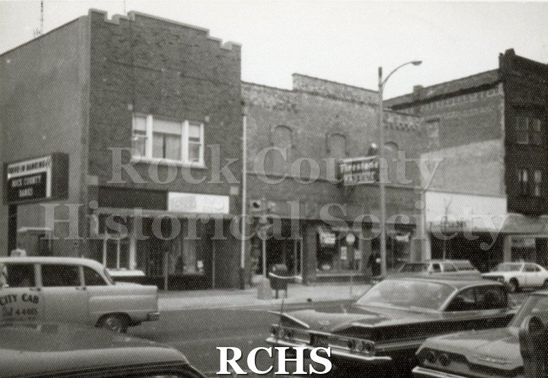 Black and white photograph of downtown Janesville businesses. Visible is a sign for Firestone.