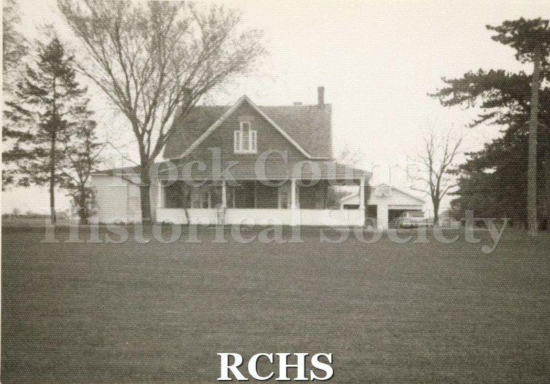 Black and white photograph of an unidentified house on Center Avenue with a porch in front and a two car garage in the back.
