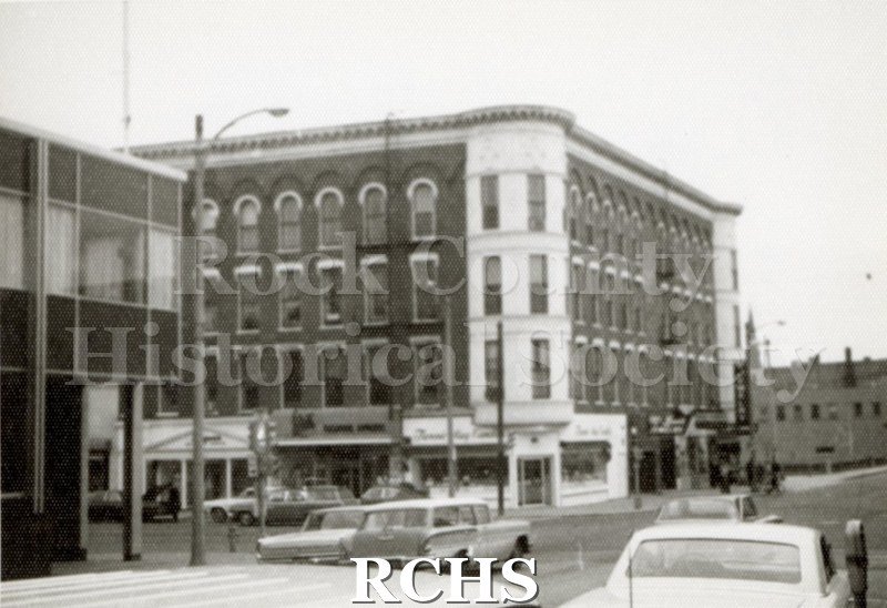 Black and white photograph of the Hayes Building in downtown Janesville.The Hayes Block is on the corner with a sign for "Fanny Mae Candies" visible.