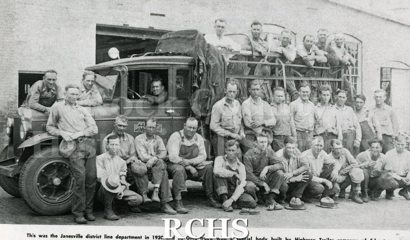 Historic image of Black and white copy print of several men standing beside, sitting on the ground and standing in the bed of a truck.