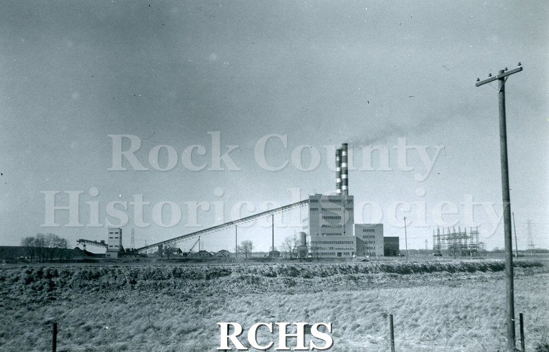 Black and white photograph of the Rock River Generating Plant WPL, an electrical generating plant, shown from a distance.