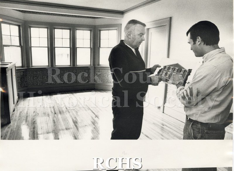 Black and white photograph of Paul Power and Paul Holznecht in an interior room with a model of a house in their hands.
