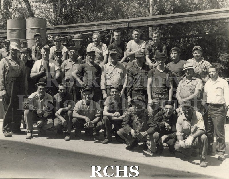 Black and white photograph of several men standing and sitting on a sidewalk. They are workers from the Highway Trailer who are being phased out.