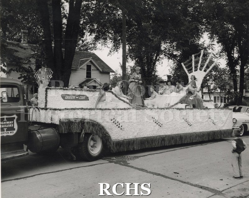 Black and white photograph of a parade float pulled by a Highway Trailers truck. On the float is a sign: "Queen and Court" .