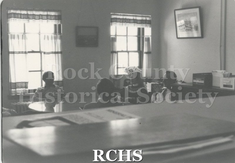 Black and white photograph of an interior room with four people sitting around a round table.